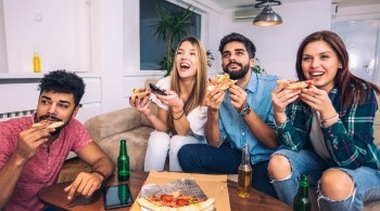 A group of friends watching TV and eating pizza